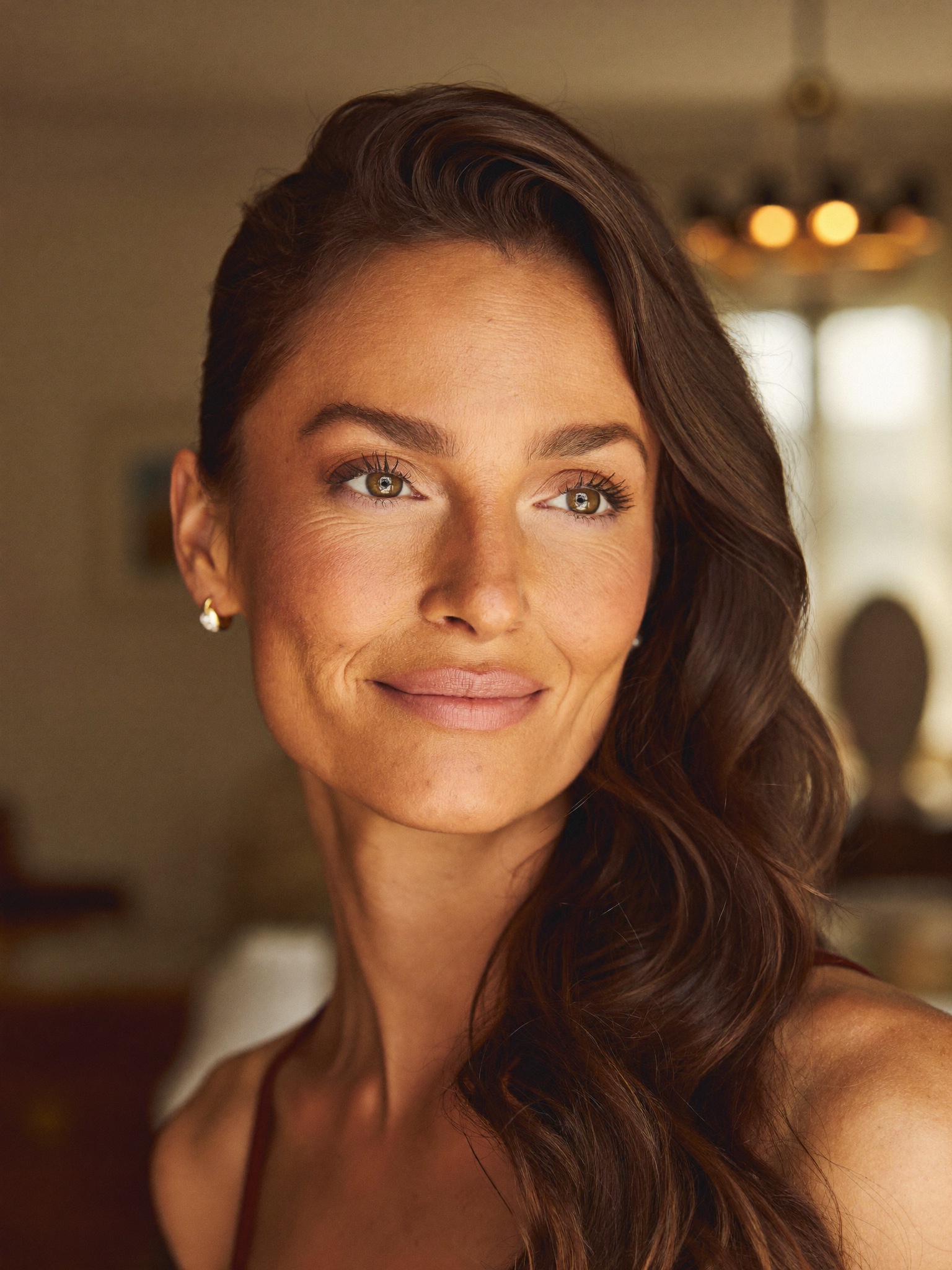 A refined woman in warm natural light with open, rested, naturally refreshed eyes — looking quietly confident