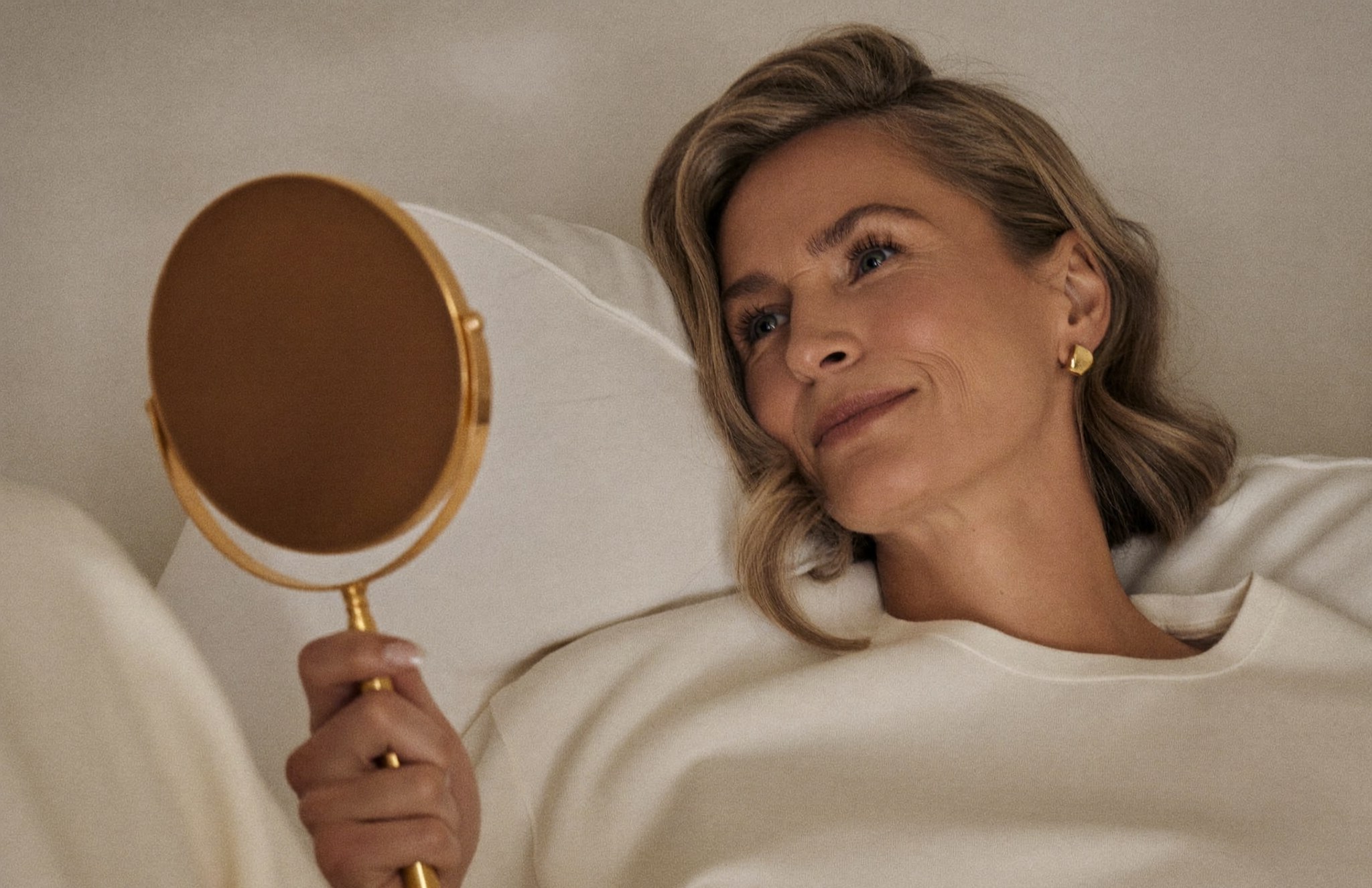 A woman at ease at home, looking at her refreshed, rested eyes in a small hand mirror
