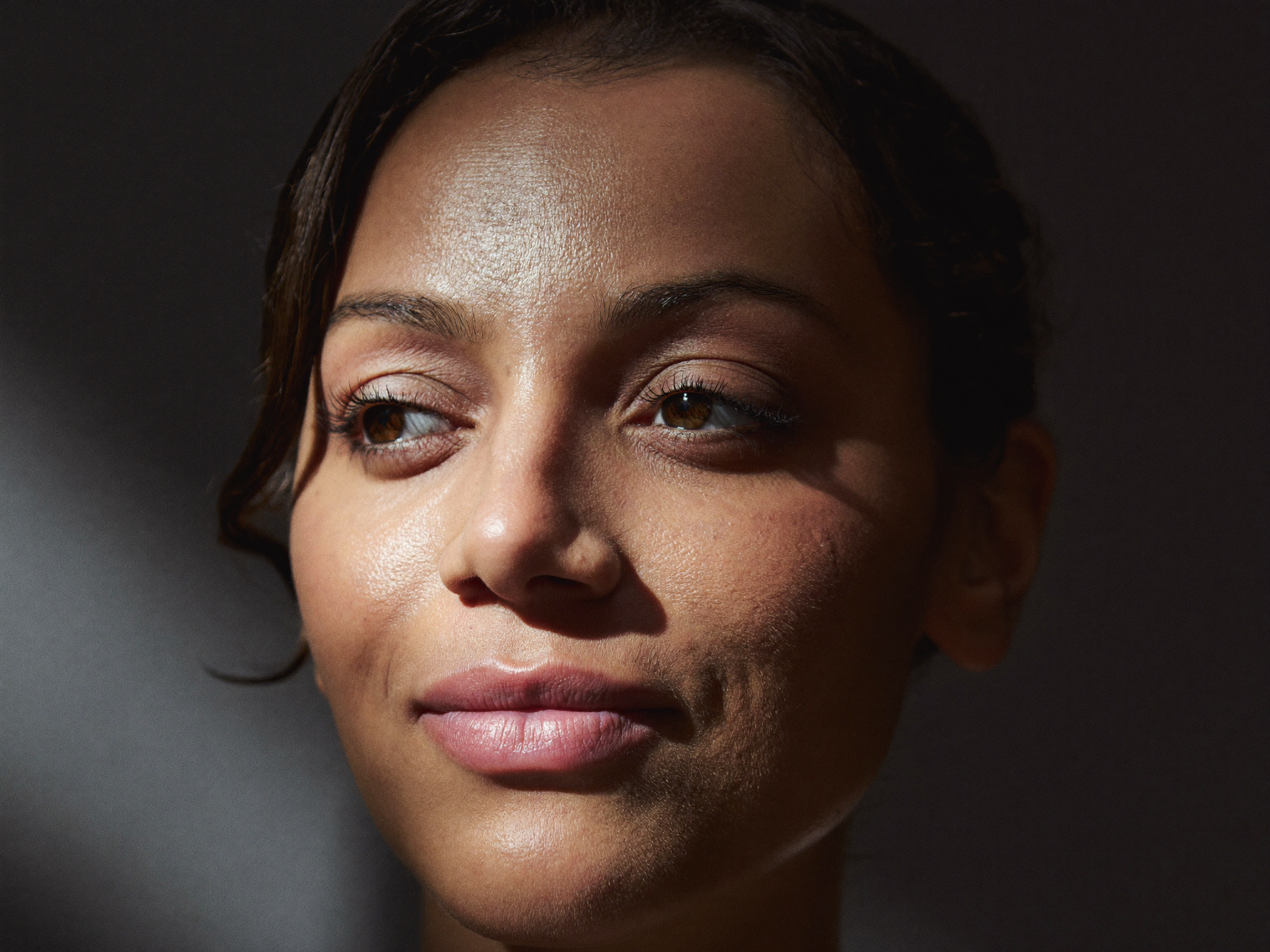 A close editorial portrait of a woman's bright, rested, naturally open eyes in dramatic soft light